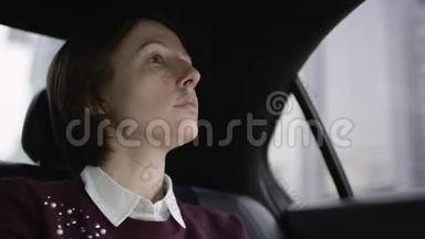 美丽的女人，棕色头发，穿着白色衬衫和栗色毛衣，坐在车里看着窗户